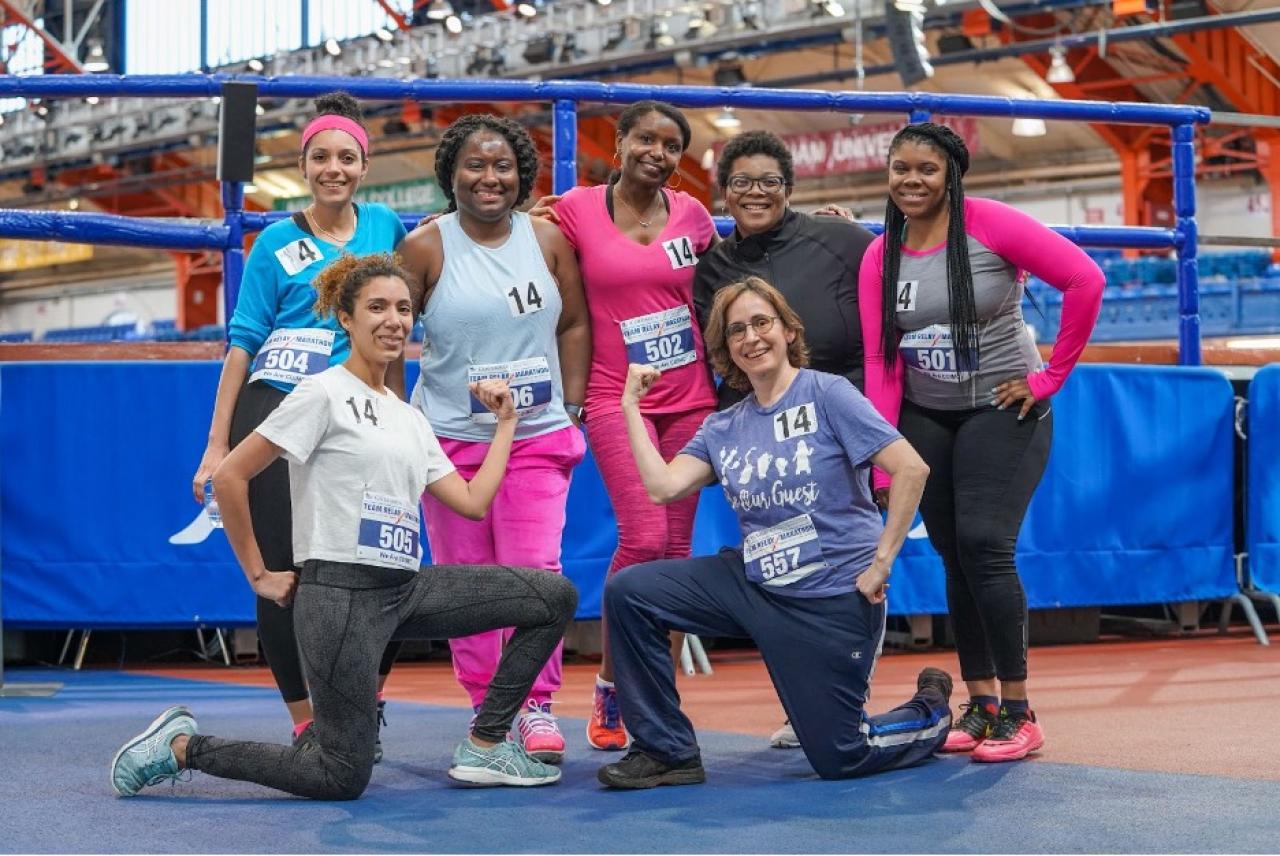 seven women runners pose for a team picture next to a running track
