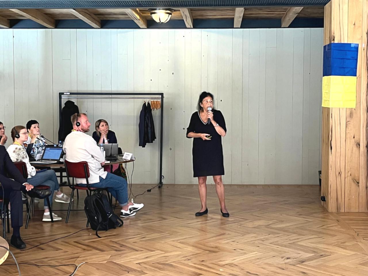 woman standing and speaking to a group of seated people