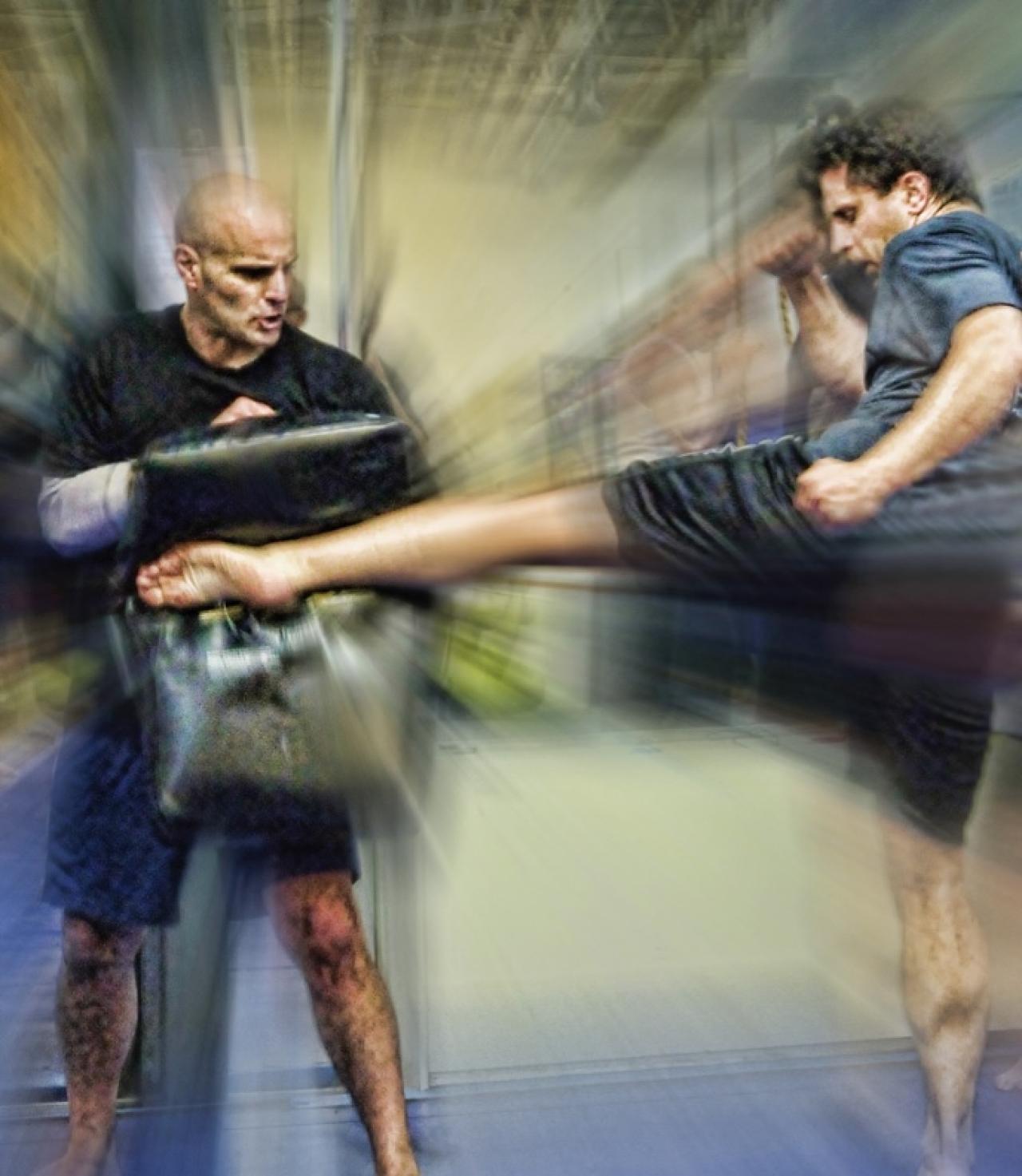 man in martial arts studio kicking a pad