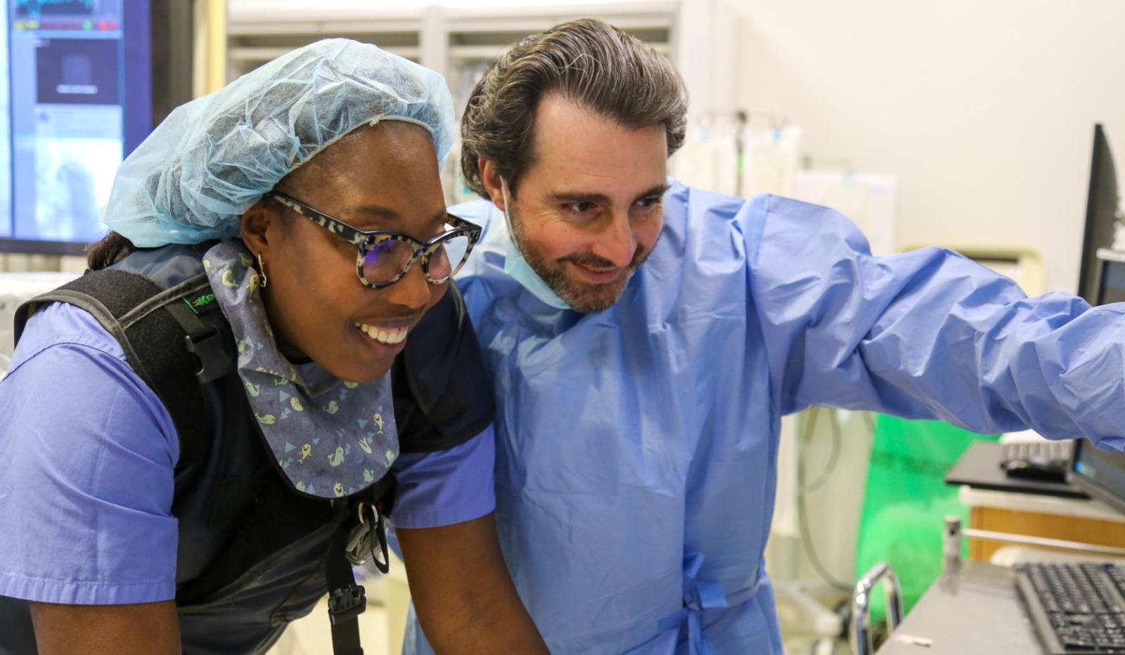 two doctors in scrubs looking at patient data on a screen