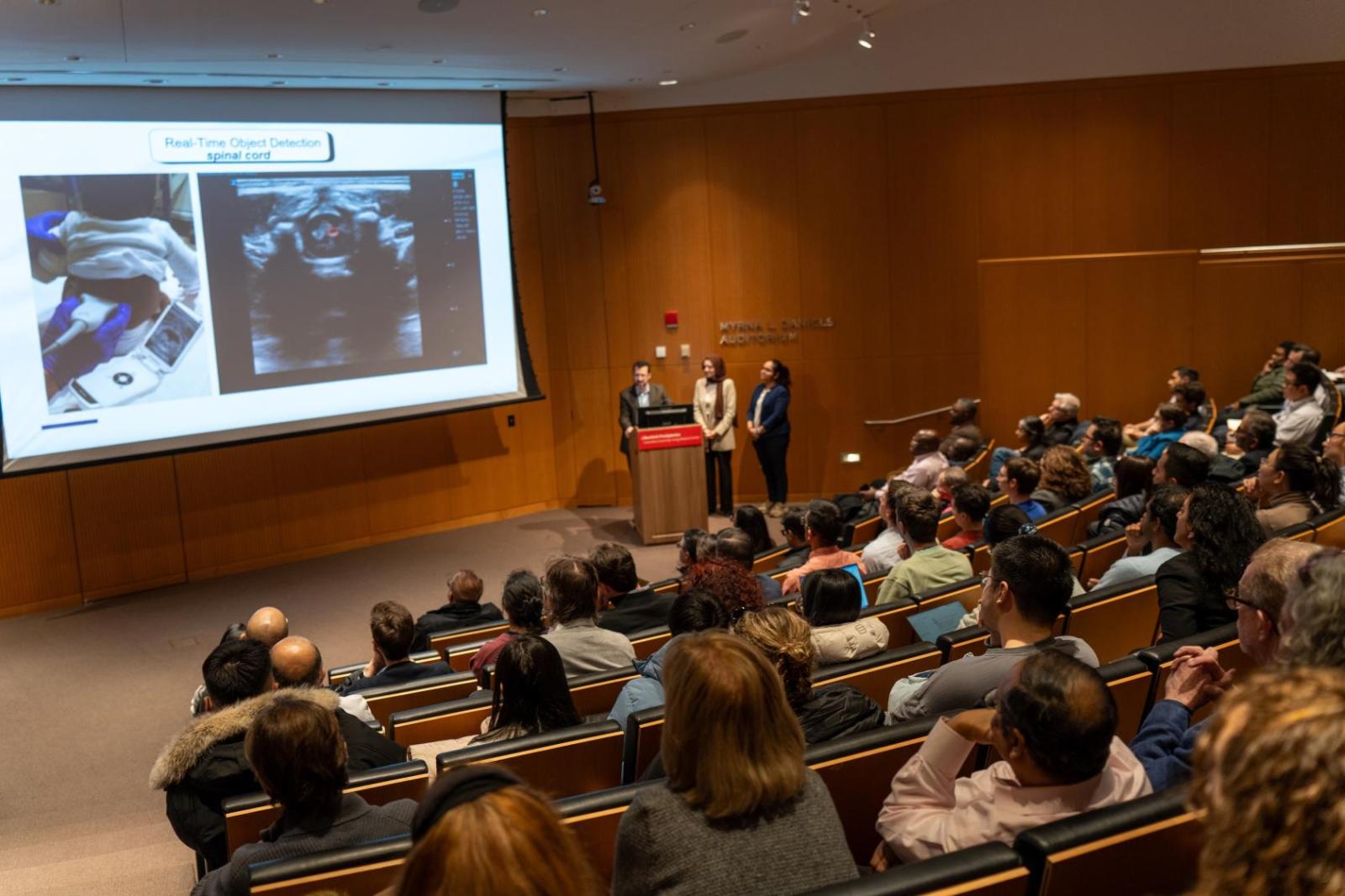 people in auditorium watching speakers at a podium