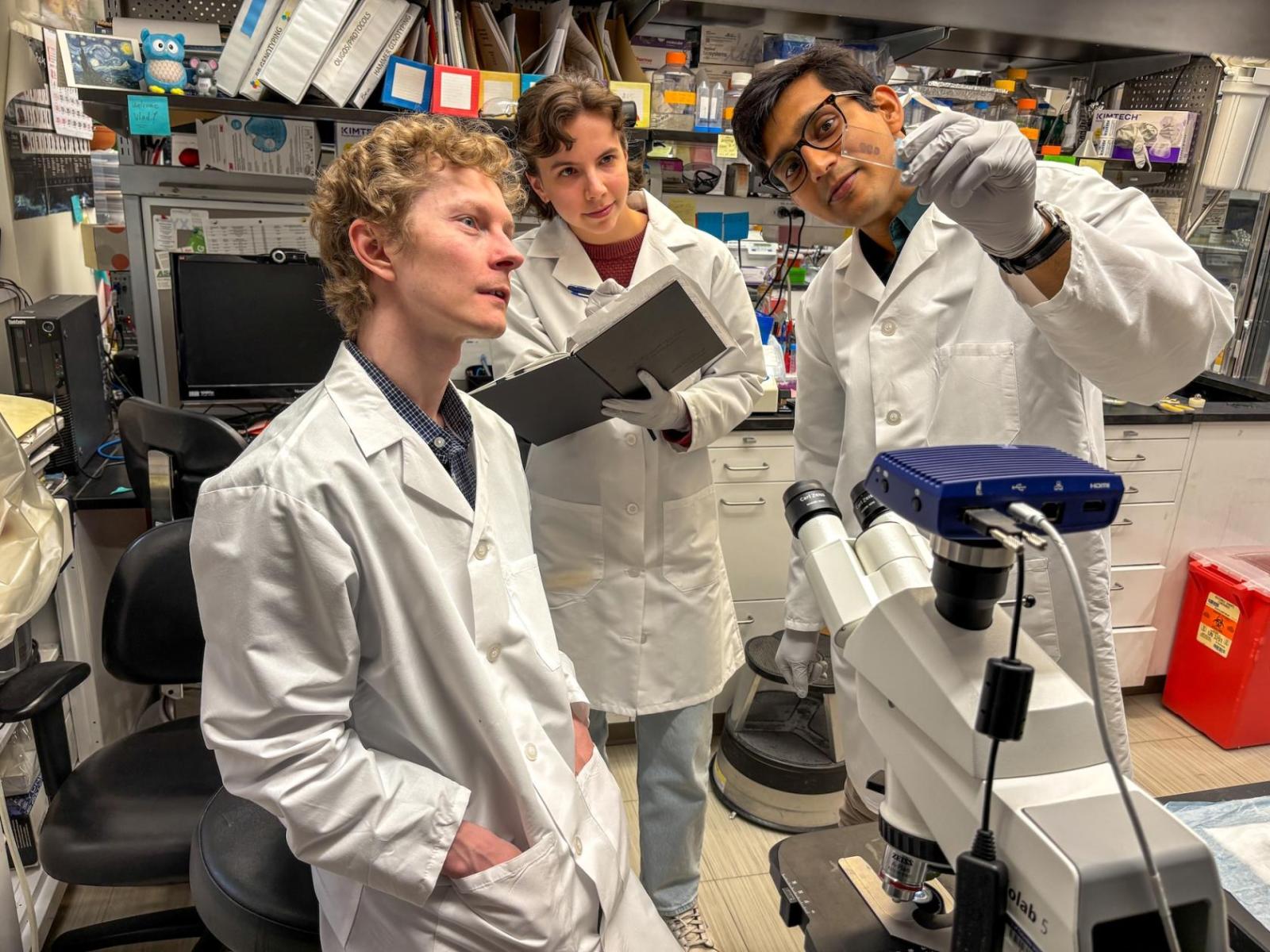 three scientists with a slide and microscope in a laboratory