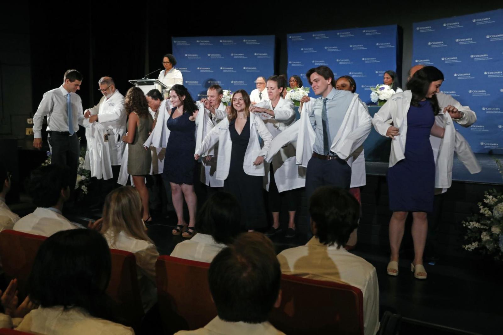 medical students donning white coats during ceremony