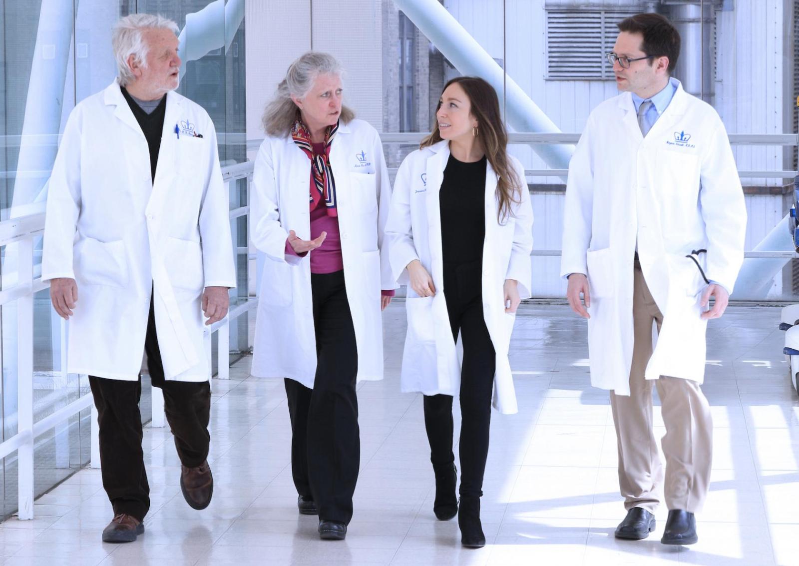 four people in white medical coats walking in a hospital hallway