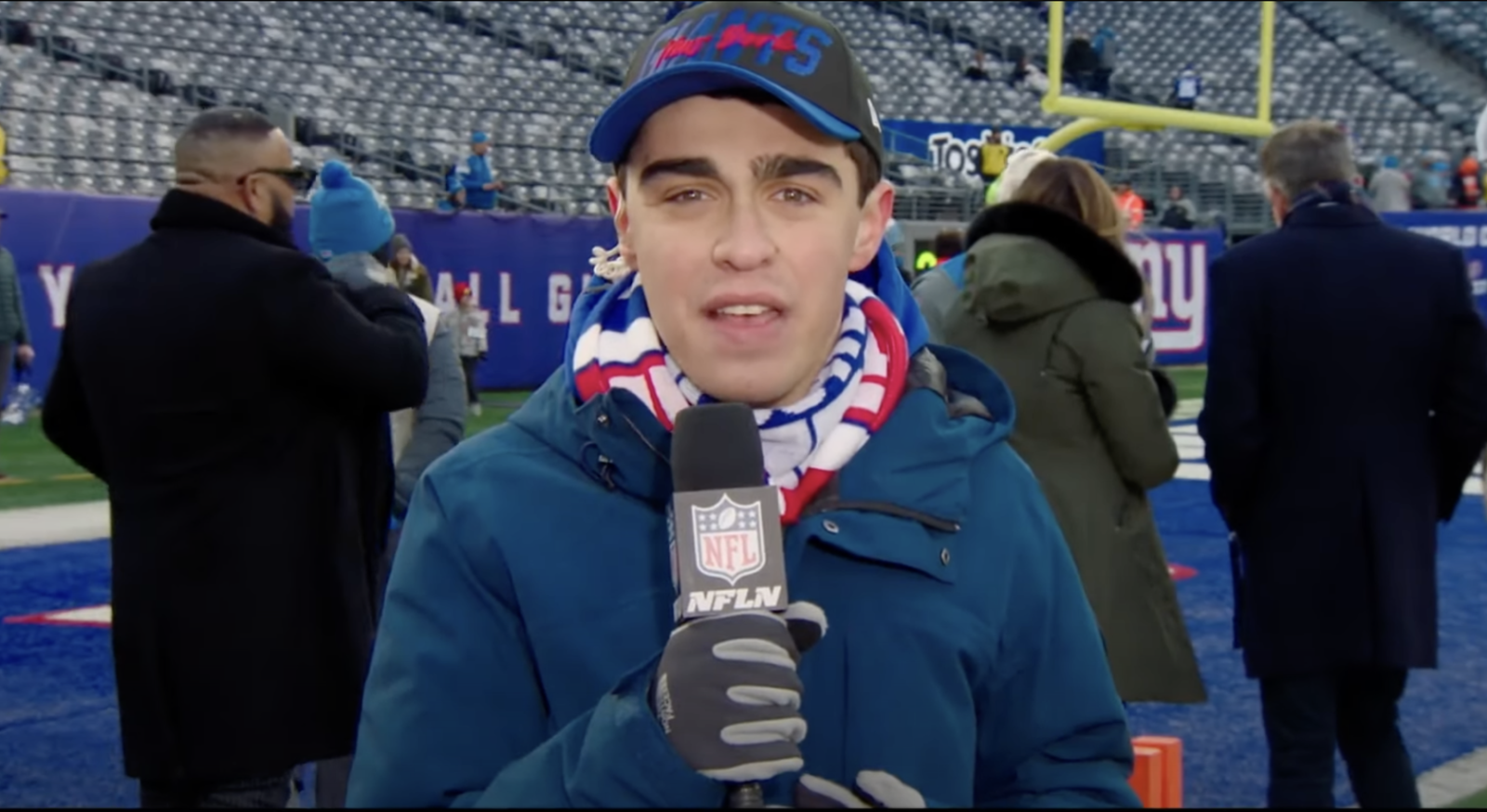 young man speaking into a handheld microphone on a football field