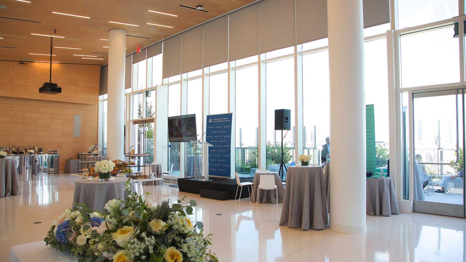 A bright reception space with floor-to-ceiling windows, catering displays, and a podium.