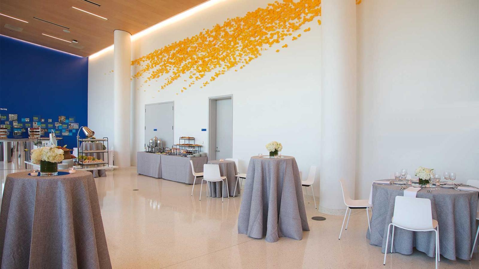 A modern event space with cocktail tables and a yellow butterfly wall installation.