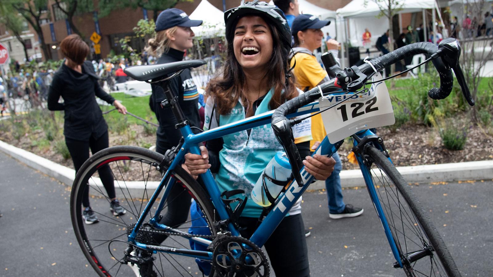 An enthusiastic Velocity rider lifts her bicycle in triumph after crossing the finish line.