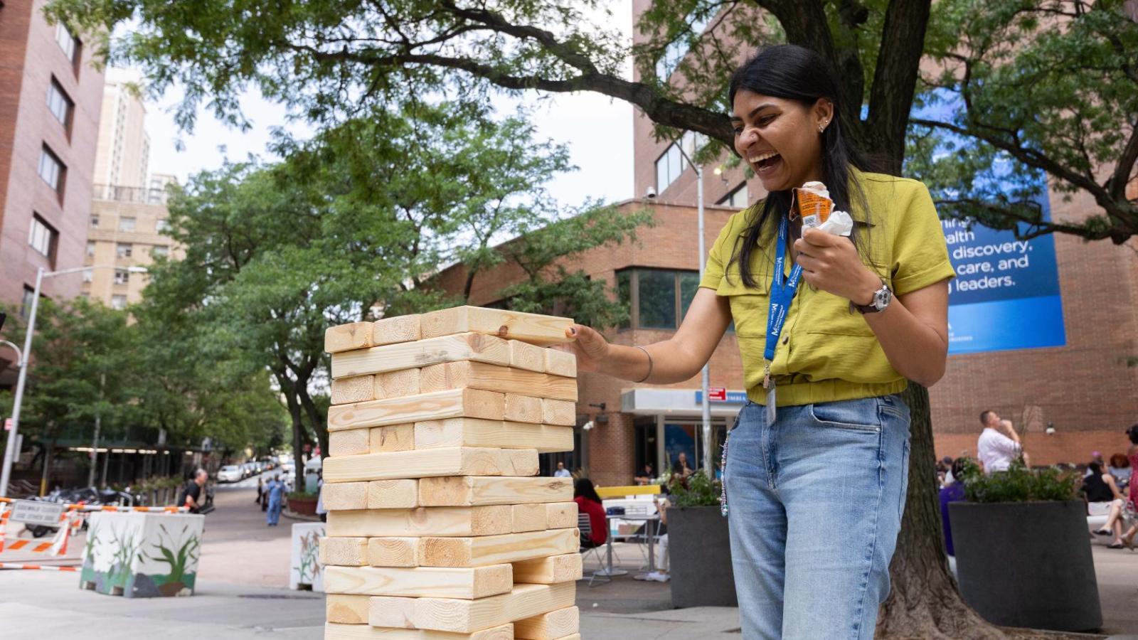 A woman plays giant jenga while holding an ice cream cone