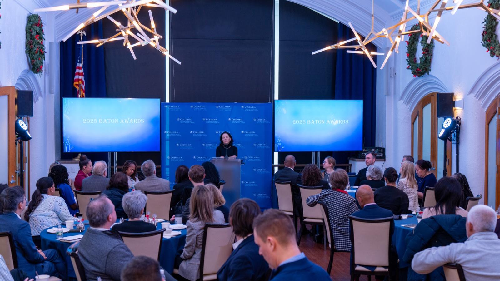 people seated watching a speaker at the front of a room