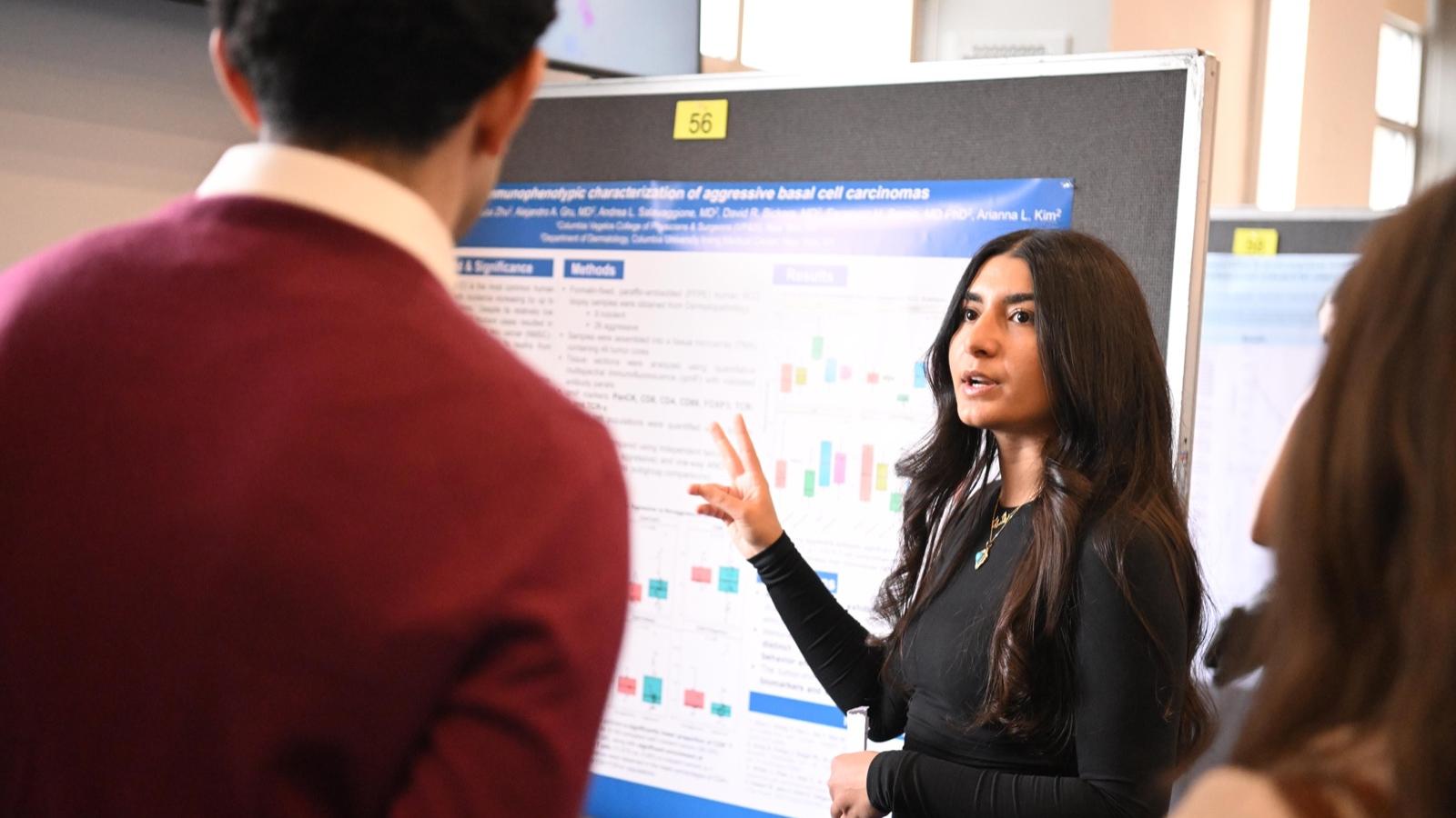 a student in front of her poster explains her research to two visitors