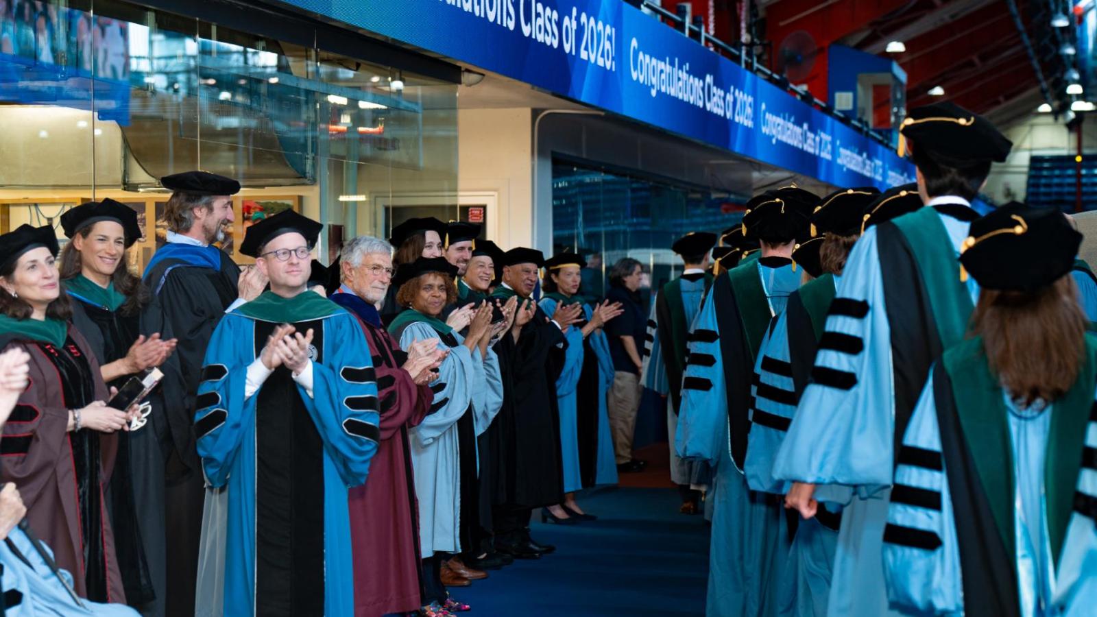 line of new graduates exiting ceremony to applause from faculty