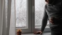 man looking sad by the window on a snowy day