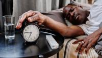 man in bed turning off his alarm clock