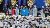 graduating students walk across a stage to receive diplomas