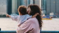 woman holding small child outside with Manhattan skyline in background