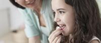 child putting a pill into her mouth with mother watching
