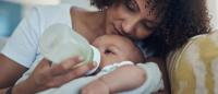 woman cradling and feeding infant with bottle of formula