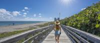 vacation person in sun hat walking on boardwalk beside beautiful Atlantic Ocean Florida beach under blue sky