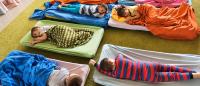 High angle view of group of tired kids in pajamas resting on beds at kindergarten.