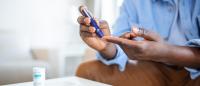 African man is sitting at the sofa at the home and taking blood from his finger due to diabetes. The daily life of a man of African-American ethnicity person with a chronic illness who is using glucose tester.