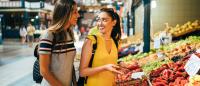 Two young women choosing vegetables at an indoor farmer’s market