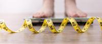 legs and feet on weight scale, close-up of yellow measuring tape; concept of losing weight