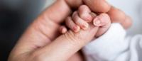 a newborn baby's fingers wrapped around thumb of adult