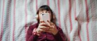 teenager lying down on bed and looking at smartphone