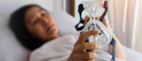Woman lies in a bed with a cpap machine in her hands