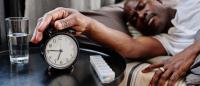 man in bed turning off his alarm clock