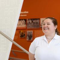 A man wearing a white polo shirt over a long-sleeved blue shirt smiles as he speaks with a young women who also is smiling and wearing the same white polo shirt