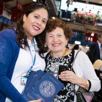 A younger woman and an older woman embrace while holding a printed blue program booklet